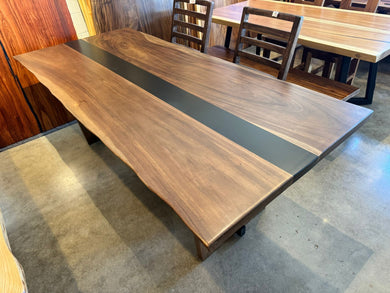 Large wooden dining table with a dark stripe in a room with chairs and another table.