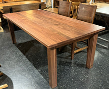 A rectangular walnut dining table with a smooth, polished surface showcasing rich brown tones and unique grain patterns. The table is supported by four sleek corner legs, offering a modern, minimalist design that adds elegance and stability to any dining space.