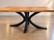 Butterfly sculptural black metal pedestal dining table base supporting a natural wood tabletop.