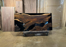 A Live Edge dining table top featuring rich, natural wood grain with raw, organic edges, contrasted by sleek black epoxy resin filling the cracks and imperfections, creating a modern and refined look while highlighting the wood’s unique beauty.