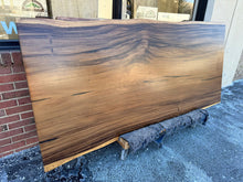 Close-up view of a live edge acacia wood slab dining table top, showcasing its natural wood grain, rich tones, and unique, irregular edges that highlight the organic beauty of the wood