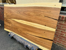 Live edge wood dining table featuring a natural, organic edge with visible wood grain and knots, supported by sturdy metal or wooden legs, blending rustic and modern design elements.