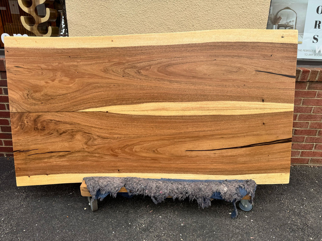 Live edge wood dining table featuring a natural, organic edge with visible wood grain and knots, supported by sturdy metal or wooden legs, blending rustic and modern design elements.