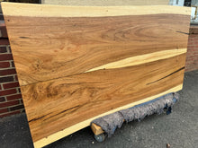 Live edge wood dining table featuring a natural, organic edge with visible wood grain and knots, supported by sturdy metal or wooden legs, blending rustic and modern design elements.