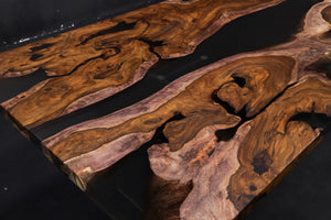 A Live Edge Dining Table Top made from Ironwood, featuring a rich, dark wood grain with natural, raw edges, complemented by an opaque black epoxy resin filling that contrasts beautifully with the wood. The epoxy creates a sleek, modern finish, highlighting the unique characteristics of the wood while adding a contemporary touch.