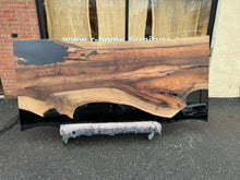 A Walnut wood dining table top featuring rich, dark brown tones and striking grain patterns, enhanced with black epoxy resin filling the natural cracks and imperfections. The smooth, polished surface showcases the contrast between the wood’s organic beauty and the sleek, modern black epoxy.