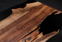 A Walnut wood dining table top featuring rich, dark brown tones and striking grain patterns, enhanced with black epoxy resin filling the natural cracks and imperfections. The smooth, polished surface showcases the contrast between the wood’s organic beauty and the sleek, modern black epoxy.