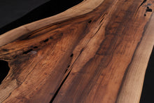 A Walnut wood dining table top featuring rich, dark brown tones and striking grain patterns, enhanced with black epoxy resin filling the natural cracks and imperfections. The smooth, polished surface showcases the contrast between the wood’s organic beauty and the sleek, modern black epoxy.
