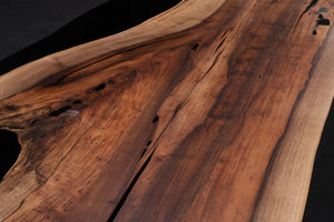 A Walnut wood dining table top featuring rich, dark brown tones and striking grain patterns, enhanced with black epoxy resin filling the natural cracks and imperfections. The smooth, polished surface showcases the contrast between the wood’s organic beauty and the sleek, modern black epoxy.