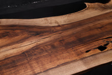 A Walnut wood dining table top featuring rich, dark brown tones and striking grain patterns, enhanced with black epoxy resin filling the natural cracks and imperfections. The smooth, polished surface showcases the contrast between the wood’s organic beauty and the sleek, modern black epoxy.