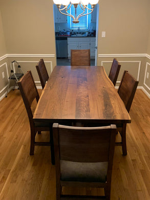 A walnut brown dining table with six chairs around it, placed in a room with light beige walls and a light wood floor.
