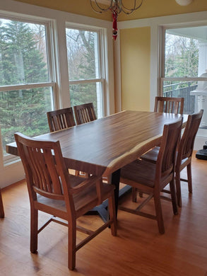 A wooden dining table with four chairs around it, placed in a room with a window and a decorative Christmas tree in the background.
