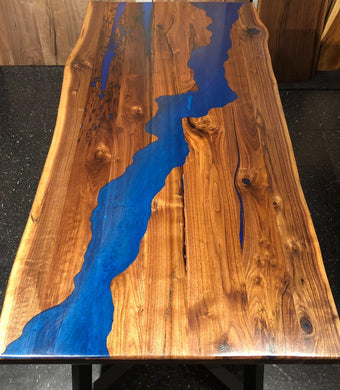 A live edge dining table with a walnut wood slab top and a river-like blue epoxy finish on the tabletop.